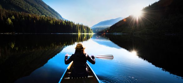 Woman in a canoe in the water looking at mountains at sunset